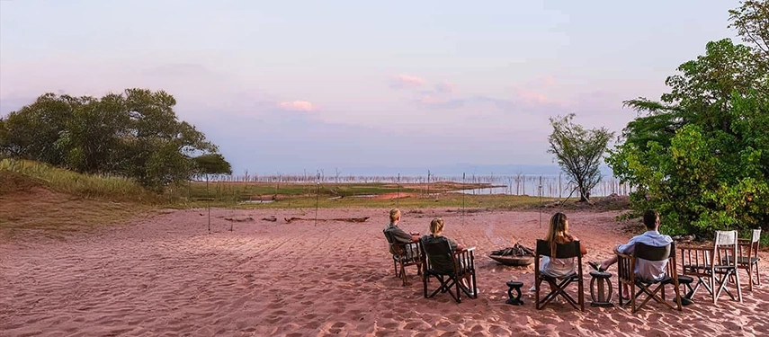 Guests seated around a firepit on the sandy shoreline of Lake Kariba, enjoying sunset views and relaxed evenings at Changa Safari Camp.