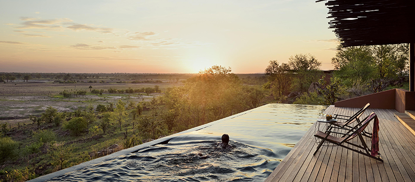 Guest swims in Chichele Presidential luxury safari Lodge infinity pool at sunset in South Luangwa National Park, Zambia