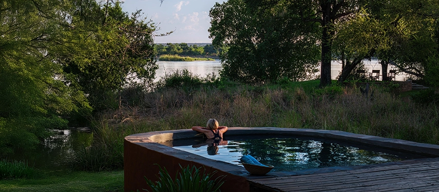 Guest relaxing in a riverside plunge pool surrounded by trees at Chundukwa River Lodge.