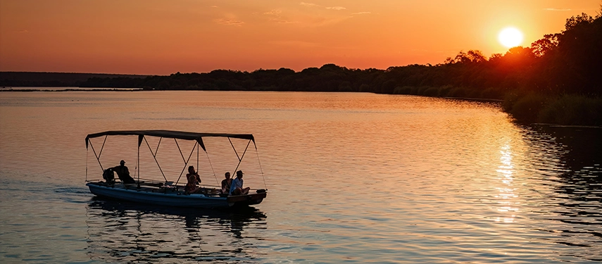 Boat gliding along the Zambezi River at sunset during a scenic lodge cruise.