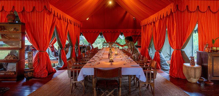 The mess tent at Mbamba Camp, elegantly set for dining under a vibrant red canopy.