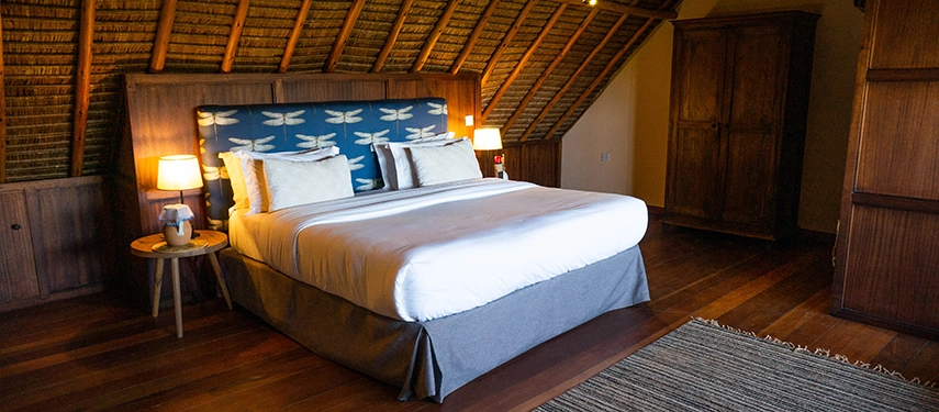 Cosy thatched-roof bedroom with a king-sized bed, dragonfly-patterned headboard, and warm wooden interiors at Ololo Safari Lodge.