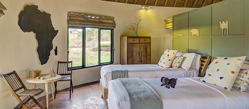 Charming twin bedroom with African-inspired décor, soft lighting, and views of the surrounding bushland at Ololo Safari Lodge.
