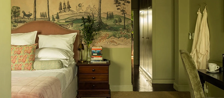 Stylish guest room at Dorp Hotel with painted forest mural, vintage wooden furniture, and soft ambient lighting.