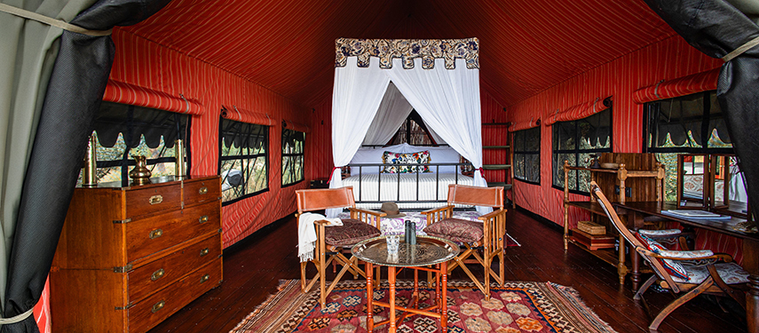 Interior of a guest tent featuring a canopy bed, vintage furnishings, and rich red decor.