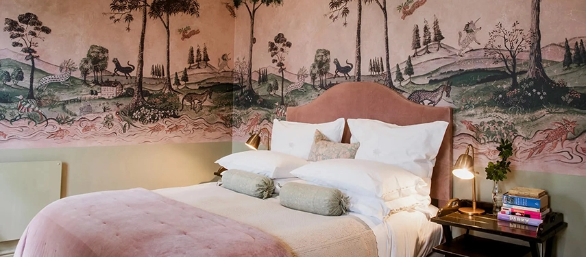 Artfully decorated Dorp Hotel bedroom with hand-painted mural walls, pink velvet headboard, and antique furnishings.