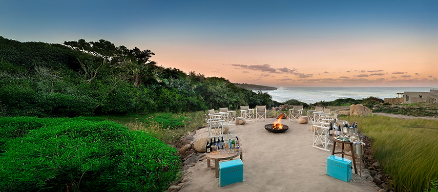 Outdoor fire pit area set up for evening drinks with views of the ocean and lush surroundings.