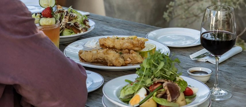 Al fresco dining at Dorp Hotel with fresh salads, crisp fish dishes, and a glass of red wine served on a rustic wooden table.