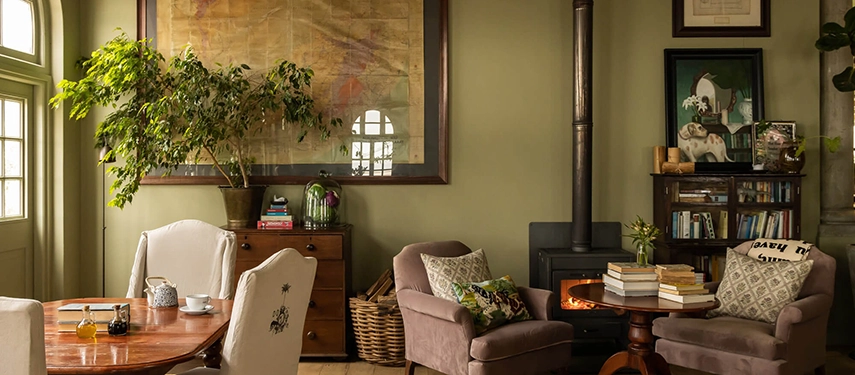 Cosy sitting room at Dorp Hotel with soft green walls, antique furnishings, and a wood-burning stove creating a warm, homely atmosphere.