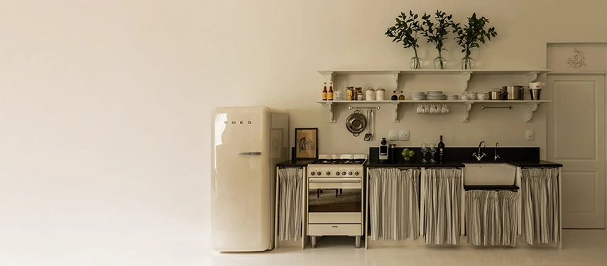 Minimalist kitchen at Dorp Hotel with a vintage cream Smeg fridge, striped linen curtains, and open shelving with curated details.