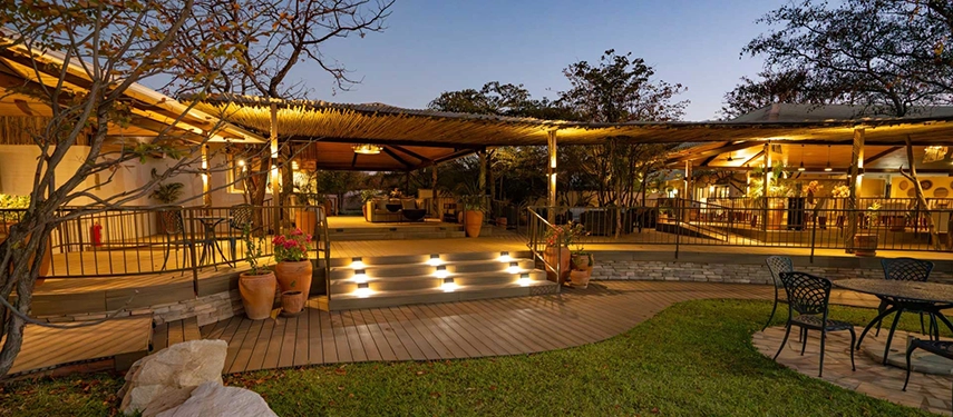 Warmly lit decked terrace with lounge and dining spaces beneath a thatched roof at Insika Lodge, Victoria Falls.