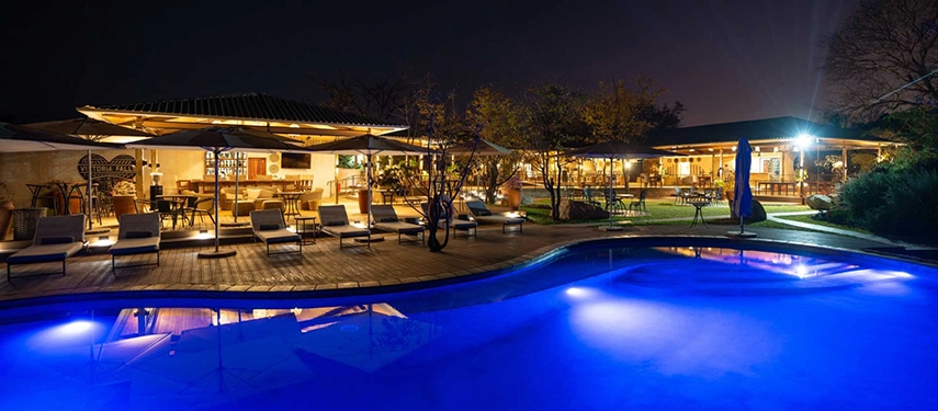 Evening view of illuminated pool deck and restaurant terrace at Insika Lodge, Victoria Falls.