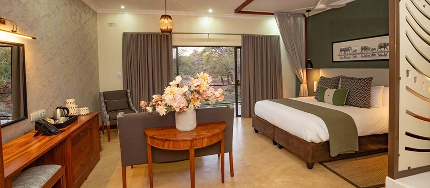 Spacious suite with fresh flowers, dining table and views through sliding doors at Insika Lodge, Victoria Falls.