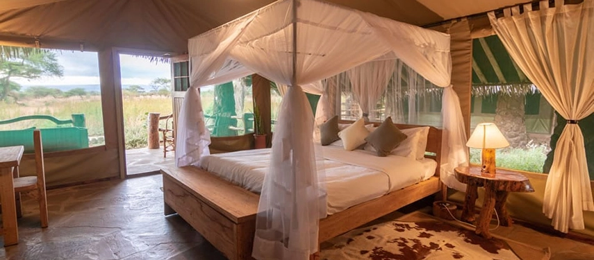 Spacious luxury safari tent with a canopied double bed, wooden furnishings, and views across the savannah from Karatu Simba Lodge.