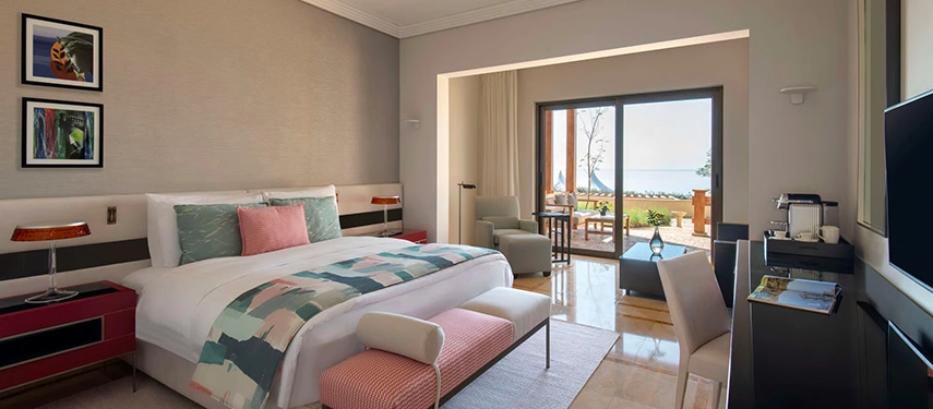A contemporary guest room with plush furnishings and floor-to-ceiling doors leading onto a private terrace facing the Dead Sea.