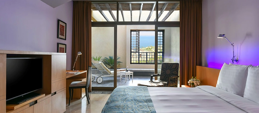 A spacious guest room opening onto a private terrace, blending contemporary comfort with Dead Sea views and soft natural light.