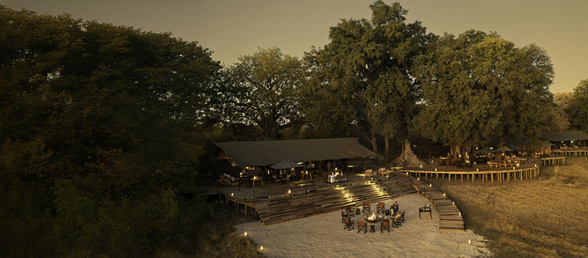 Elevated evening view of Kiri Camp with firepit seating and dining decks beneath towering trees.