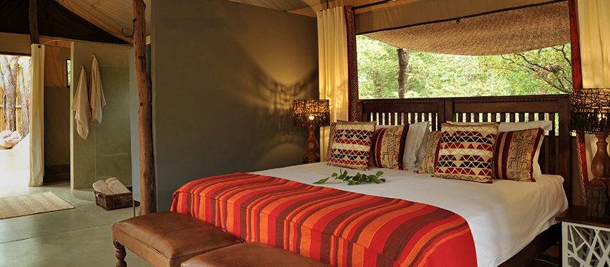 A comfortable safari tent bedroom featuring warm textiles, natural timber furnishings and an en suite bathroom open to nature.