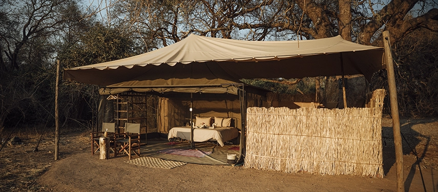 A wide view of a safari tent at Kutandala Camp shows its shaded veranda, reed screening and seamless connection to the bush.