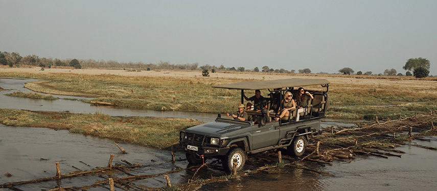 A safari vehicle carefully crosses a shallow river channel, carrying guests through the remote floodplains of North Luangwa.
