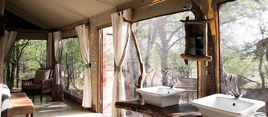 The open-air bathroom at Kutandala Camp features twin basins, natural wood finishes and canvas walls overlooking the forest.