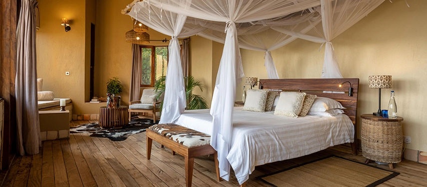 An elegant guest room at Kyambura Gorge Lodge featuring a four-poster bed, natural timber floors and soft safari-inspired furnishings.