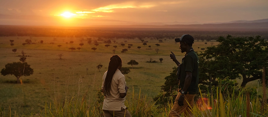 Guests and a guide pause at sunset on a ridge above Queen Elizabeth National Park, enjoying expansive savannah views near Kyambura Gorge Lodge.