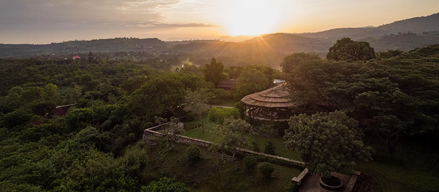 Golden sunset light illuminates Kyambura Gorge Lodge, revealing its elevated position above rolling forest and savannah landscapes.