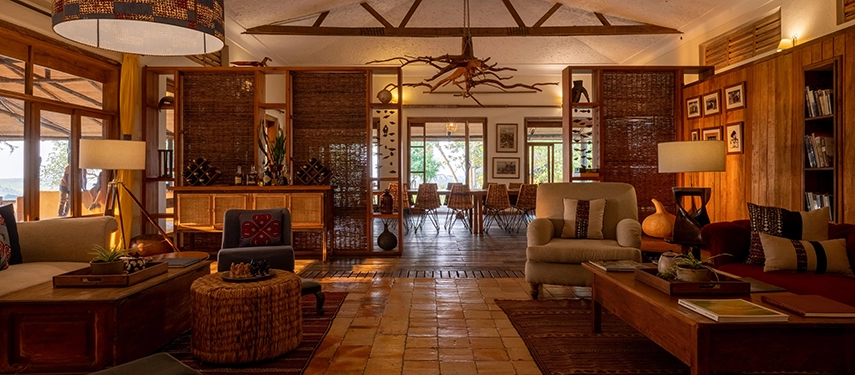 The main lounge at Kyambura Gorge Lodge blends warm timber, soft lighting and curated African details, creating a relaxed space for unwinding between activities.