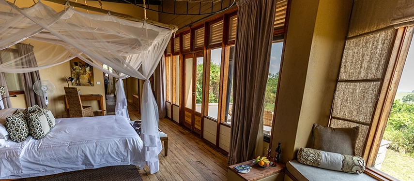 Another angle of a Kyambura Gorge Lodge guest room reveals polished timber floors, soft furnishings and panoramic views across the surrounding greenery.
