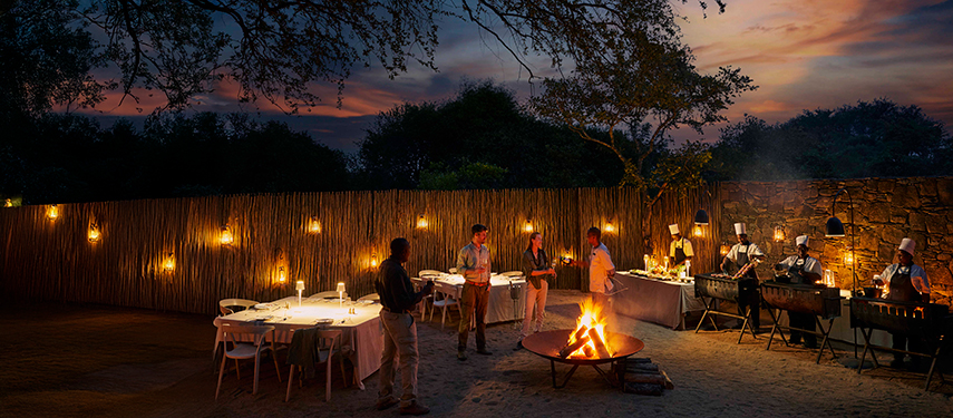 Intimate outdoor dining experience at the boma under lanterns and firelight at dusk.