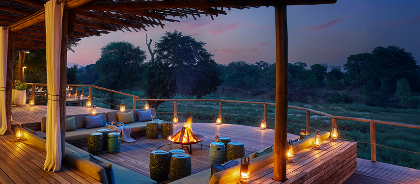 Cosy firepit lounge area on the main deck with panoramic views of the river at sunset.