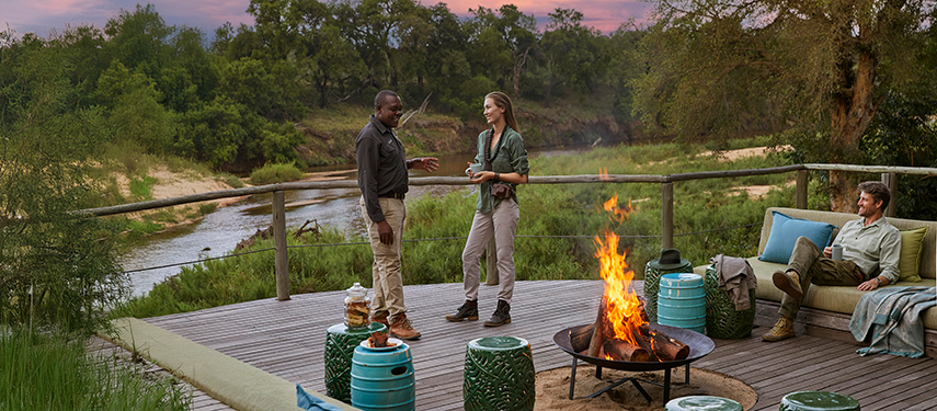 Guests relaxing around the morning firepit with coffee and river views at dawn.