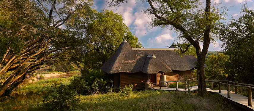 Thatch-roofed guest suite nestled in lush greenery along a wooden walkway.