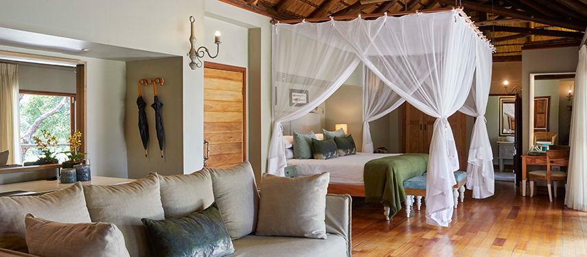 Spacious suite interior with canopy bed, lounge area and natural light filtering through large windows.