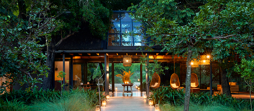 Inviting entrance to Lion Sands River Lodge lit with lanterns, surrounded by lush trees and ambient lighting.