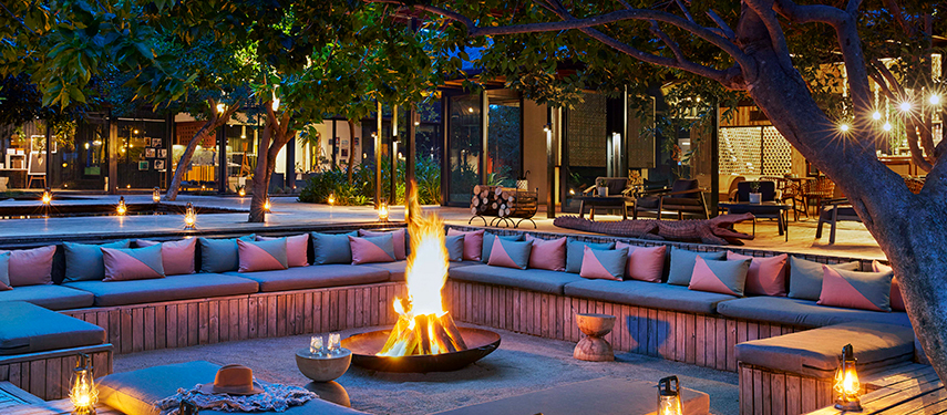 Cosy circular fire pit area at Lion Sands River Lodge, glowing at dusk with plush seating and lanterns.