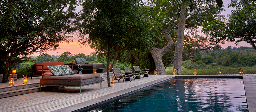 ranquil swimming pool deck at sunset with loungers, lanterns, and bushveld views.