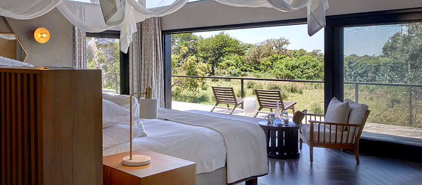 Luxurious river suite interior with large windows opening to a private deck and nature beyond.