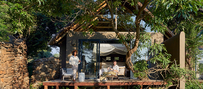 Guest enjoying the shaded veranda of a luxury suite surrounded by trees and stone walls.