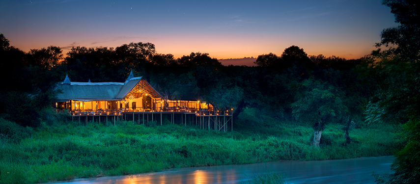 Narina Lodge glowing warmly above the Sabie River as dusk sets over the bush.