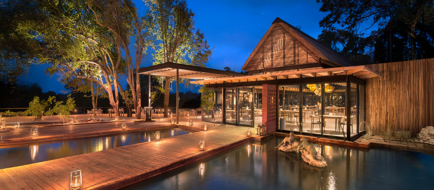 Lantern-lit wooden walkways surrounding the evening-lit dining area at Lion Sands River Lodge.