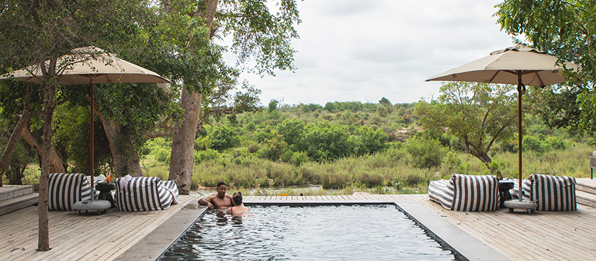 Couple relaxing on a timber deck beside a plunge pool with bushveld views.