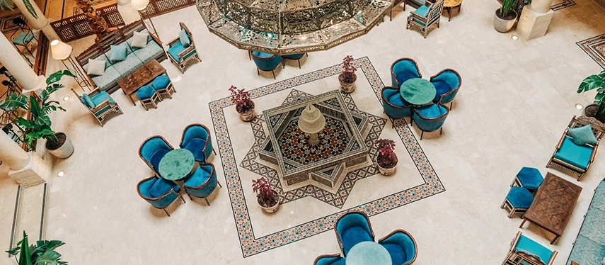 An aerial view of Mövenpick Hotel Petra’s central atrium highlights patterned stone floors, a decorative fountain and elegant turquoise seating.