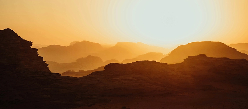 Golden light spills across the layered sandstone mountains of Wadi Rum as the sun rises over the desert horizon.