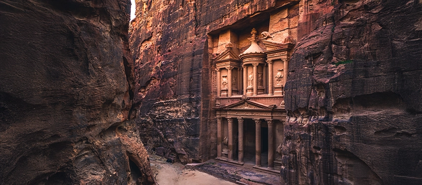 The Treasury of Petra reveals itself dramatically through the narrow walls of the Siq, its intricately carved façade glowing against dark canyon stone.