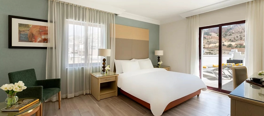 A bright and serene guest room at Mövenpick Hotel Petra opens onto a private terrace with views across the surrounding hills.
