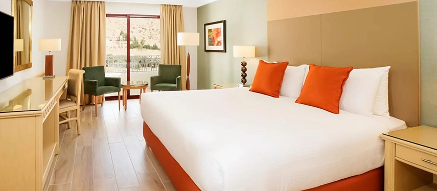 A bright and contemporary guest room at Mövenpick Hotel Petra opens onto a private balcony with views over the surrounding hills.