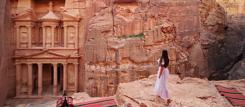 A woman gazes across Petra’s ancient Treasury from an elevated viewpoint, the monumental rock-cut façade rising from the canyon below.