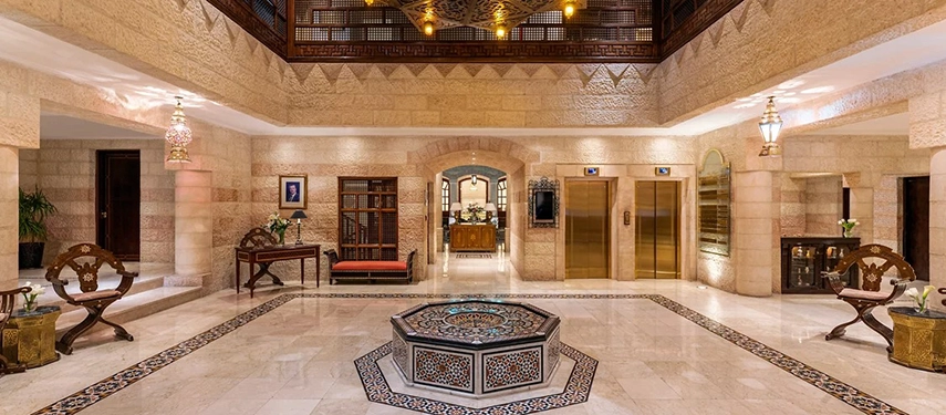 The grand atrium of Mövenpick Hotel Petra showcases Arabesque stonework, ornate lanterns and a central fountain beneath a high ceiling.